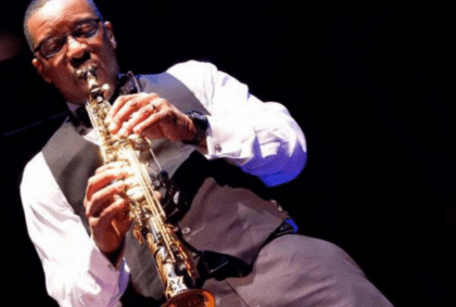 A man wearing a vest passionately plays a saxophone, showcasing his musical talent and dedication