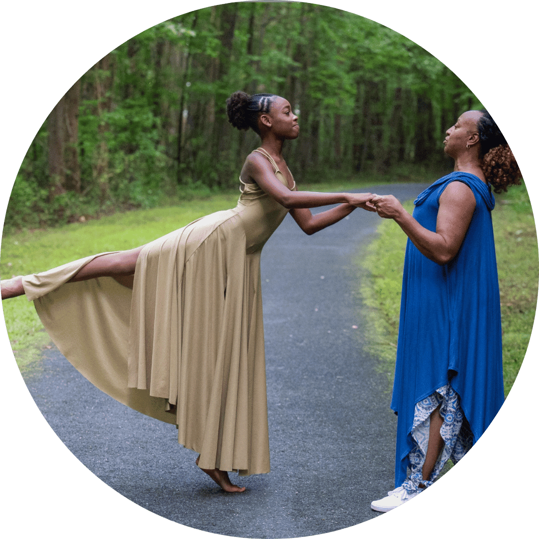 Two women in blue dresses gracefully dance together on a scenic path surrounded by nature.